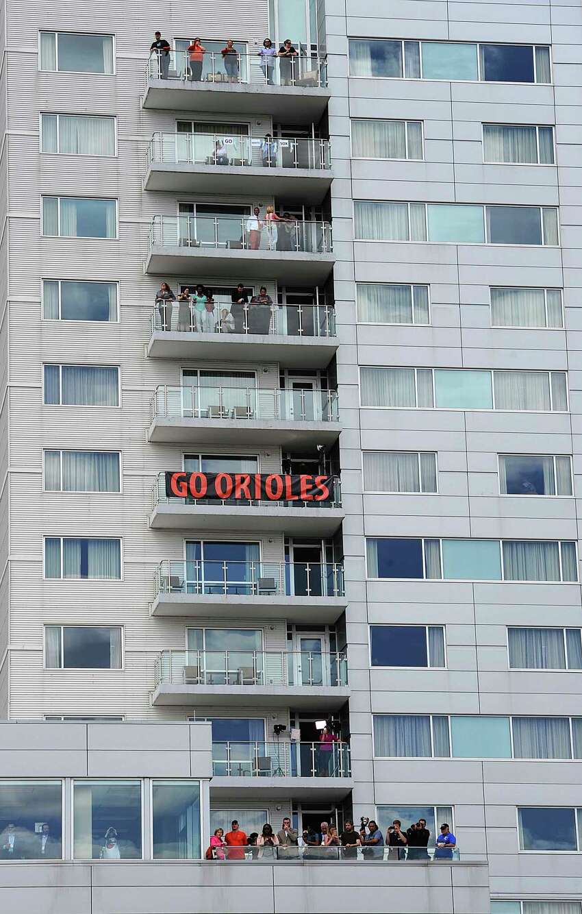 FILE - In this April 29, 2015, file photo, baseball fans watch from a hotel across the street during a baseball game between the Baltimore Orioles and Chicago White Sox that was closed to the public due to security concerns. This week, Major League Baseball players and owners reached an agreement to play an abbreviated, 60-game season that would start July 23 or 24 in teamsa€™ home ballparks. But the seats will be empty. Instead, fans hoping to see a game in person will be have to settle for pressing their faces up against hotel windows, squinting through metal grates or climb to rooftops when baseball returns this month in otherwise empty stadiums. (AP Photo/Gail Burton, File)
