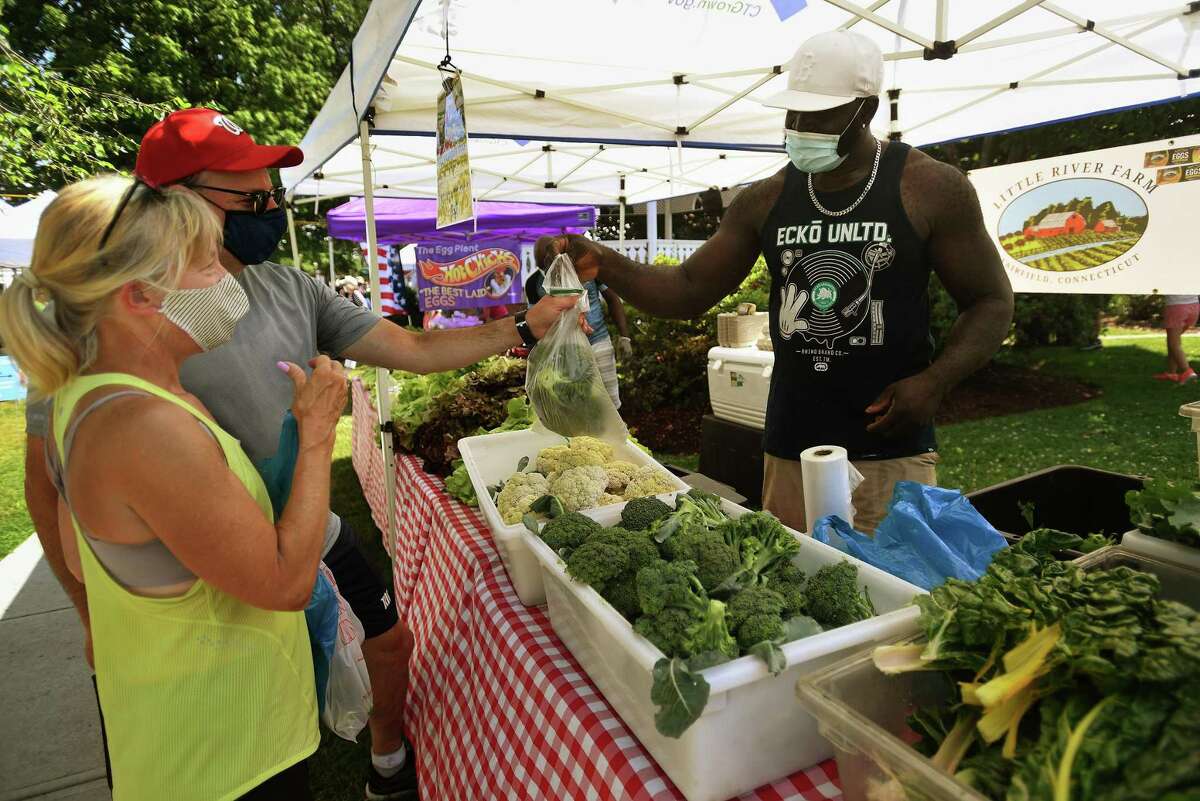 Lisa and Len Wolin, of Fairfield, purchase fresh produce from Octavious Stoddart of Little River Farm in Fairfield during the opening day of the Fairfield Farmers Market on Sherman Green on Sunday, June 28, 2020. at right, customers browse among the produce tables.