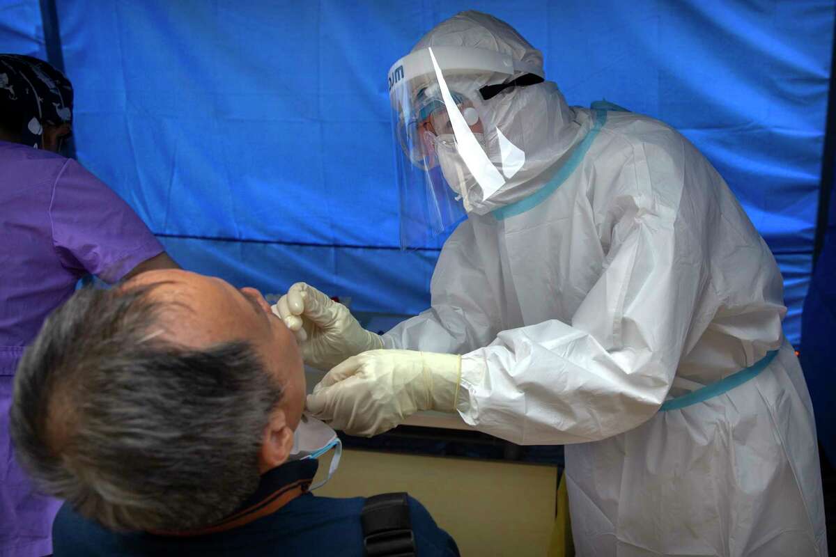 A worker wearing a protective suit swabs a man's throat for a coronavirus test at a community health clinic in Beijing, Sunday, June 28, 2020. China reported more than a dozen of new confirmed cases of COVID-19 on Sunday, all but a few of them from domestic transmission in Beijing, which has seen a recent spike in coronavirus infections. But authorities in the Chinese capital say a campaign to conduct tests on employees at hair and beauty salons across the city has found no positive cases so far, in a further sign that the recent outbreak has been largely brought under control. (AP Photo/Mark Schiefelbein)