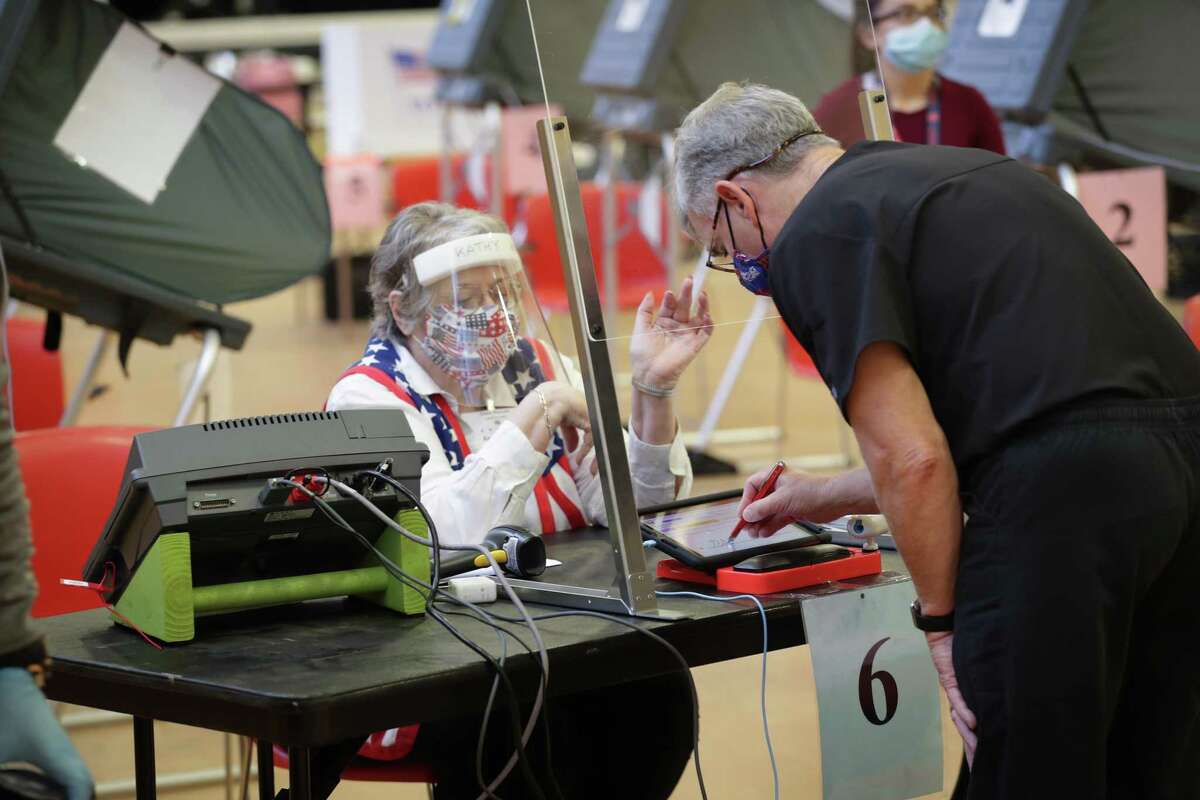 Kathy Kellen sits behind and wears a plastic shield and face covering as she helps an early voter at in the Metropolitan Multi-Services Center, 1475 W Gray St., Monday, June 29, 2020, in Houston.
