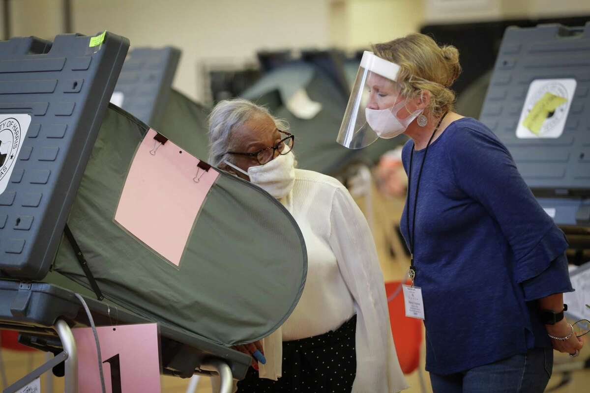 A.J. Official Marcia Ferguson (right) wears a plastic shield and face covering as she helps an early voter at in the Metropolitan Multi-Services Center, 1475 W Gray St., Monday, June 29, 2020, in Houston.