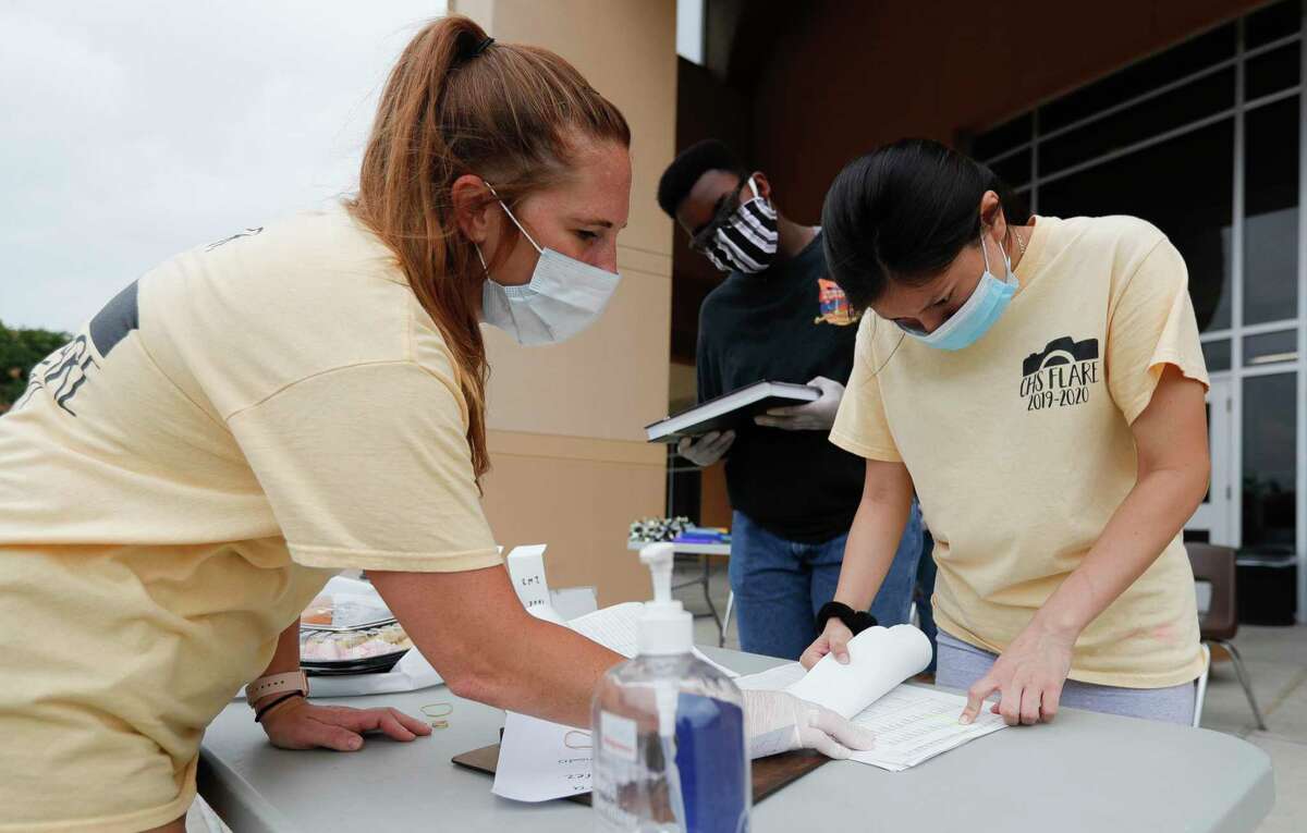 Yearbook advisor Karen Gold, left, checks a list with Xiuneli Rios, right, as Alexander Ivery looks on as staff with the Conroe High School yearbook hand out books to students, Tuesday, July 30, 2020, in Conroe. The staff handed out 625 yearbooks to students through a drive-thru line that began at 8 a.m.