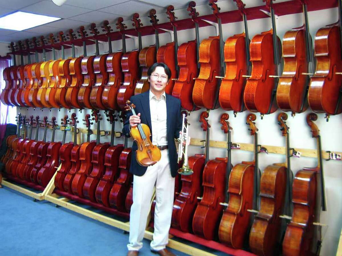 Kenneth Kuo, founder of Connecticut School of Music, stands in front of a row of cellos at the Connecticut School of Music in Westport. Kuo is launching a store in Greenwich as well.