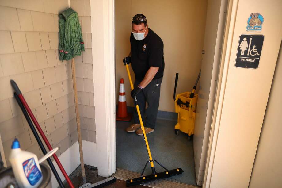 A recent study suggesting that the coronavirus could potentially spread through aerosol droplets rising from a toilet flush has led some to fear using public restrooms. Pictured: A Department of Public Works worker washes the floor of the public women's room at Mayflower Beach, and also disinfects it with cleaner as he helps to get the the restrooms open for the season in Dennis, MA on May 13, 2020. Photo: Boston Globe/Boston Globe Via Getty Images / 2020 - The Boston Globe