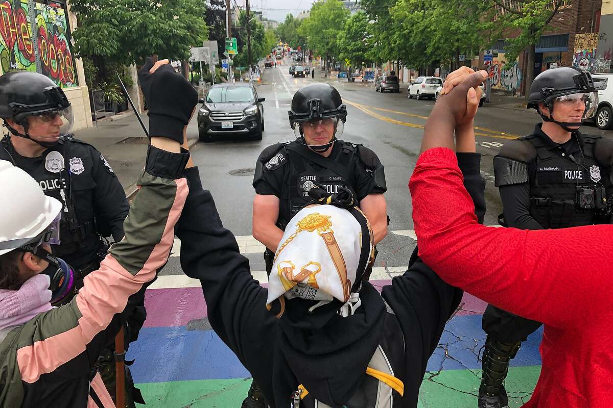 Protesters stand holding up their arms in front of a road blocked by police in the Capitol Hill Organized Protest zone early Wednesday, July 1, 2020, in Seattle. Police in Seattle have torn down demonstrators' tents in the city's so-called occupied protest zone after the mayor ordered it cleared. (AP Photo/Elaine Thompson)