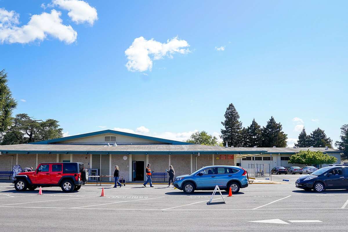 Parents wait in their car as they pick up Chromebooks at Laurelwood Elementary school so their children can use them at home to attend online classes in the Santa Clara Unified District during the coronavirus outbreak on Thursday, March 26, 2020, in Santa Clara, Calif.