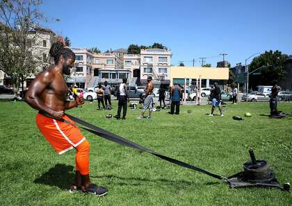 Fitness instructor Brendan Bailey pulls weights as he works out at Lakeshore Park in Oakland.