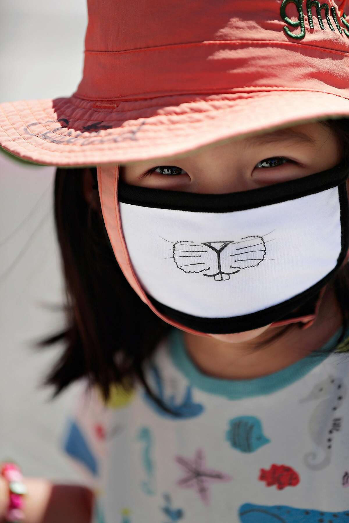 Astrid Chen smiles as she wears a mask with her mom in Monclair Village in Oakland, Calif., on Tuesday, June 30, 2020. As more positive test results show a spike in the coronavirus infections, people wanting to get outside are wearing masks to prevent the spread of the disease.