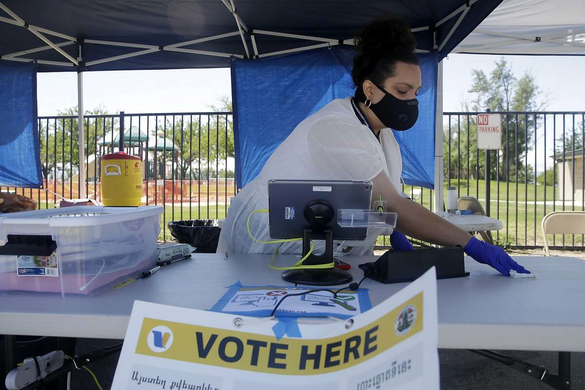 FILE - In this May 12, 2020, file photo, election worker Laura Herrera disinfects her station at a mobile voting site amid the coronavirus pandemic during a special election in Lancaster, Calif. California will establish hundreds of in-person voting places across the state for the November election, even in a year when every registered voter will be sent a mail-in ballot because of health concerns over the coronavirus. Counties must have at least one voting location per 10,000 registered voters. Statewide mail-in voting has been criticized by national Republicans as a possible pathway to large-scale voter fraud.(AP Photo/Marcio Jose Sanchez, File)