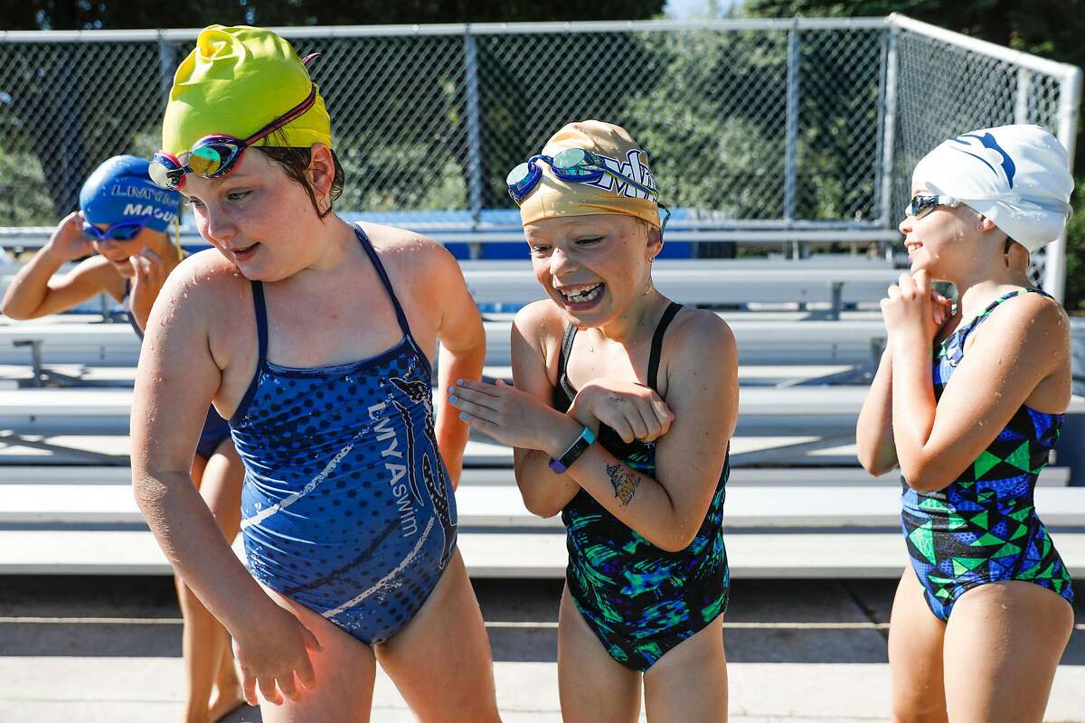 (L-r) Sydney Tumilty,8, Gwen Muldoon, 8, and Scarlett Benbow, 8 try to keep warm before jumping into the pool during swim camp at Soda Aquatic Center at Campolindo High School in Moraga, California on Thursday, July 2, 2020.