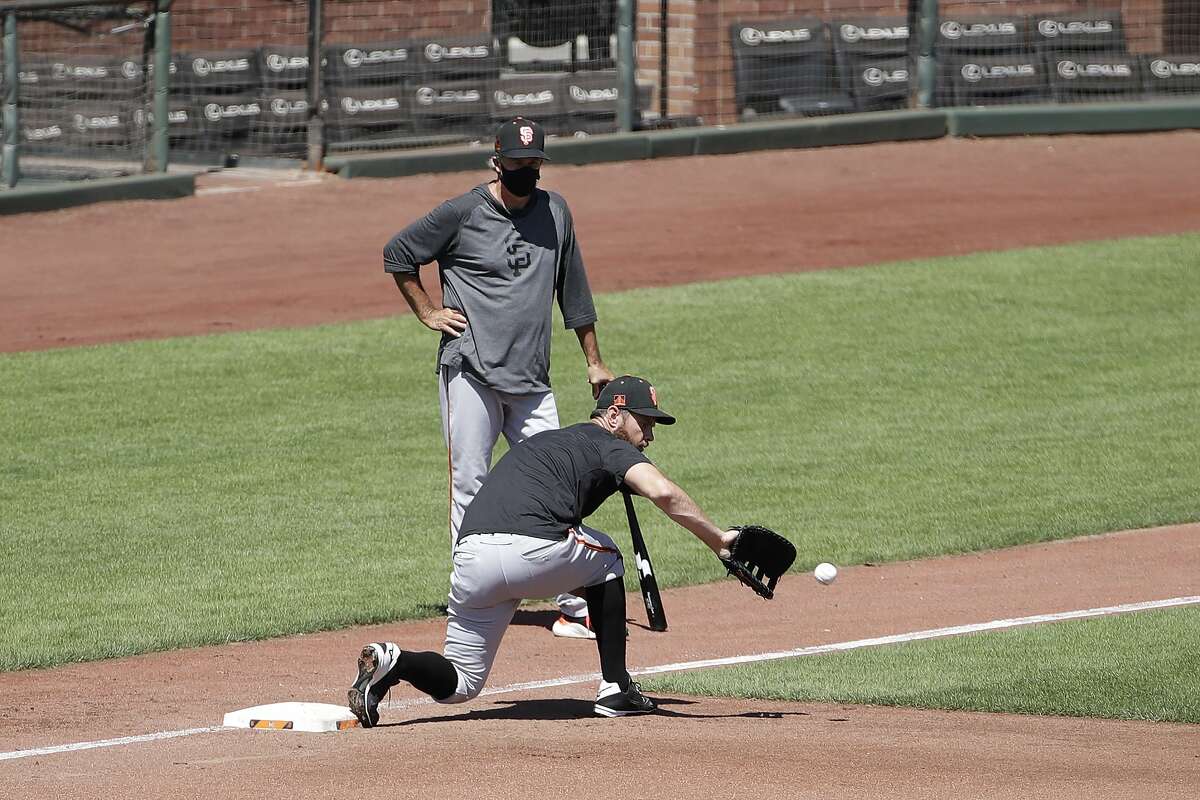 San Francisco Giants first baseman Brandon Belt, bottom, fields a ball in front of assistant coach Ron Wotus during a baseball practice in San Francisco, Sunday, July 5, 2020. (AP Photo/Jeff Chiu)