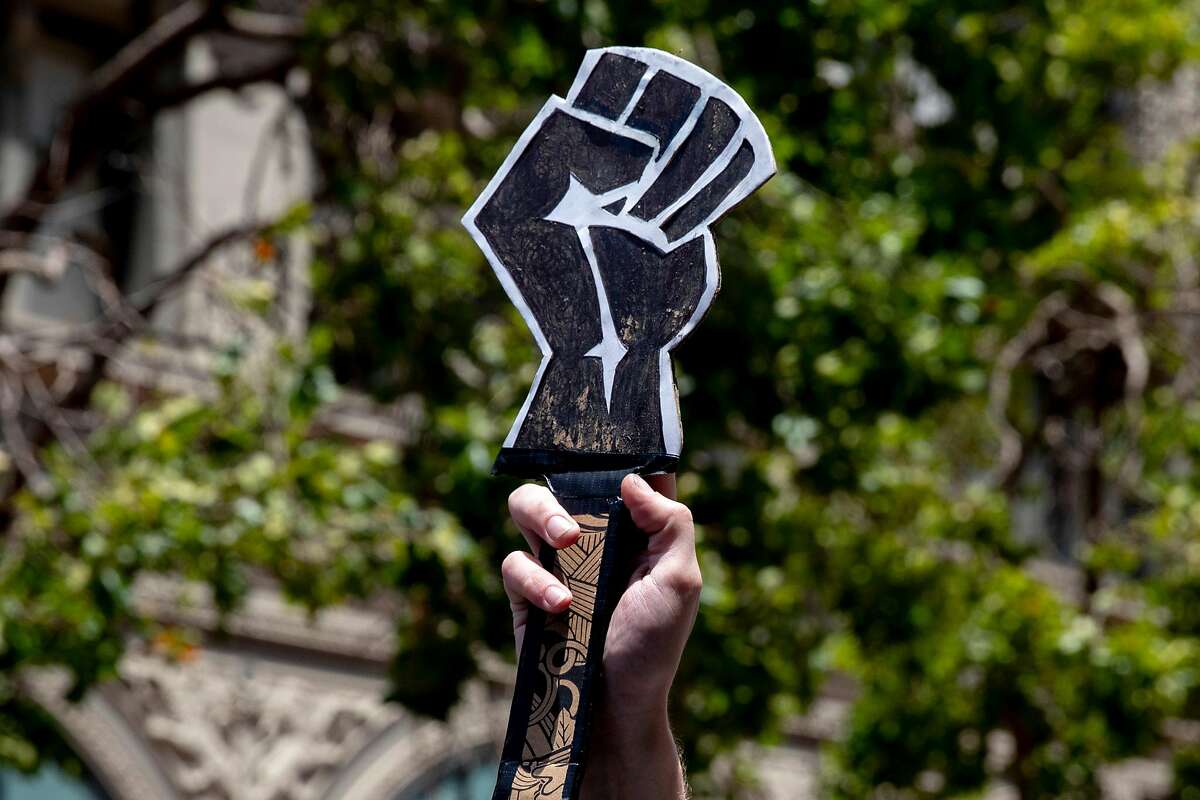 A man carries a sign depicting a Black fist while marching alongside hundreds of demonstrators down Market Street from the Ferry Building in solidarity with the Black Lives Matter movement, calling for the defunding of police, investment in Black communities and the resignation of President Trump held in San Francisco, Calif. Saturday, June 20, 2020.