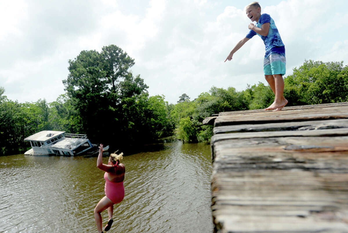 Brody Lonion laughs as his mother Ashley Ply joins stepbrother Kaden Ply jumping from the old bridge that spans Cow Bayou near the boat launch beneath the Texas 87 bridge. Ashley Ply said jumping off the old bridge into the bayou is a long tradition for kids in the area. "And especially now with places closed due to COVID-19, it's one of the only places kids have to swim" during hot summer days, she says. Ply remembers many days spent with friends when she was a teen making the over 20-foot jump, but it took some prodding from her sons to join them now. "I used to do this all the time when I was 16," she says, peering over the edge of the bridge to the water below. "Wow, this is really high!" She didn't remember it looking that high when she was a teen, she said. Eventually, the boys' pleas for her to join them in just one jump, and promises of a back massage and manicure, won her over, and the three made the jump together. Photo taken Tuesday, June 30, 2020 Kim Brent/The Enterprise