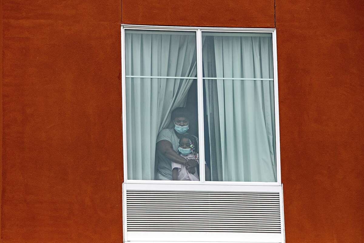 An asylum-seeking Haitian mother and her 3-year-old daughter look out the window of the room at a Homewood Suites by Hilton in San Antonio where they were being held by Immigration and Customs Enforcement on July 1, 2020. The father and son, 7, in the family are being held in a separate room.