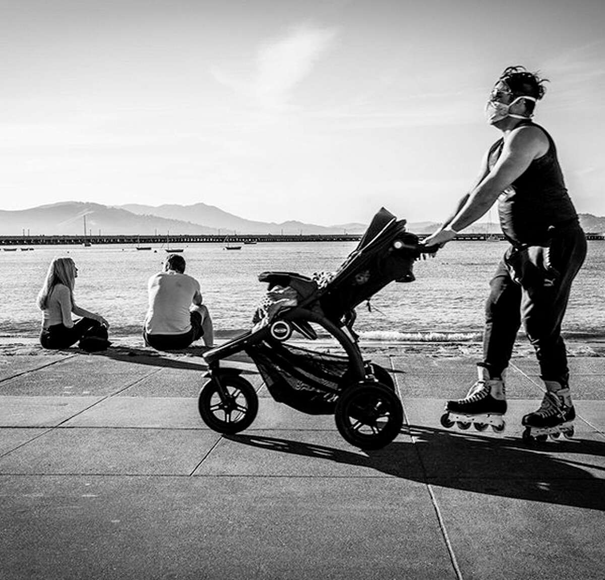 @buza_photography captured this image, "Roller Baby!" on day 41 of the shelter-in-place order in San Francisco. In this frame, the couple to the left were talking about being unemployed while the gentleman in the foreground skating by tries to preserve some semblance of an average day save the mask.