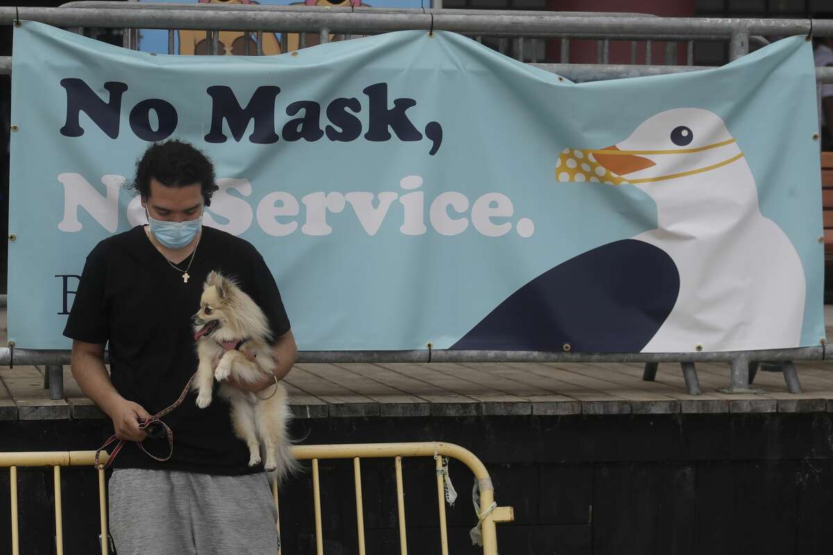 FILE: A man and his dog stop in front of a sign at the Santa Cruz Beach Boardwalk during the coronavirus outbreak in Santa Cruz, Calif., Thursday, July 2, 2020.
