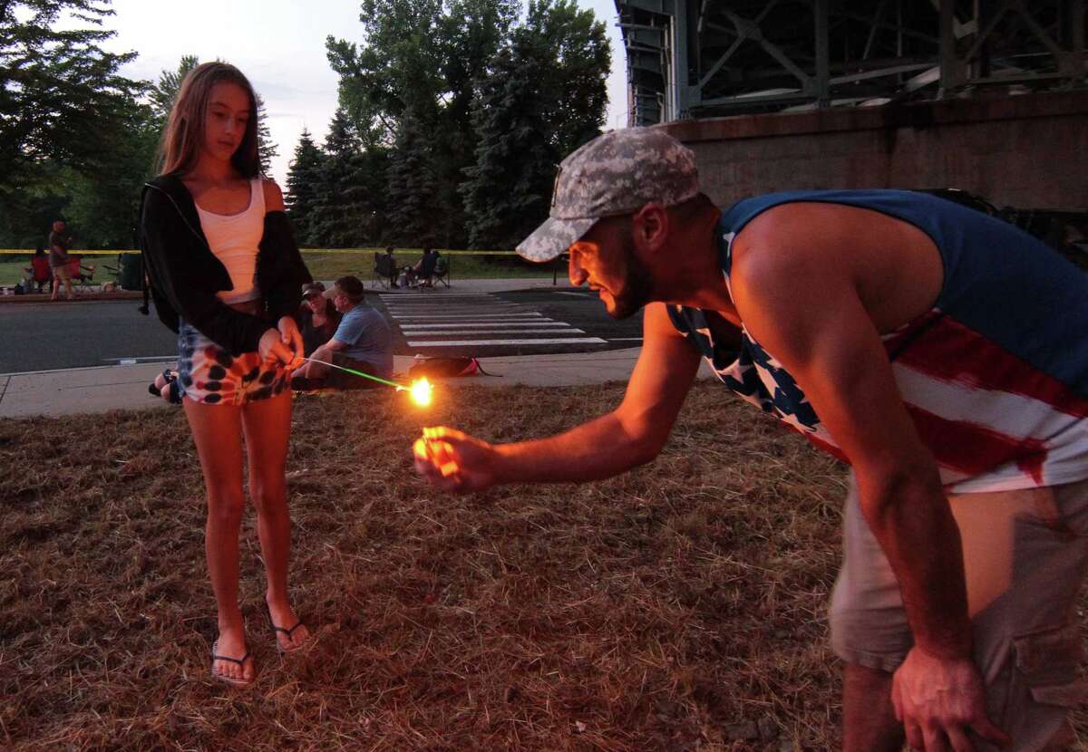 Junior Vieira, of Trumbull, lights up a sparkler for family friend Aubrey Sprague, 12, before the start of the July 4th holiday fireworks display at Veterans Memorial Park in Shelton, Conn., on Wednesday July 8, 2020. Due to the coronavirus pandemic, crowds weren't allowed to gather in the park, but were able to watch from the roads and homes nearby.