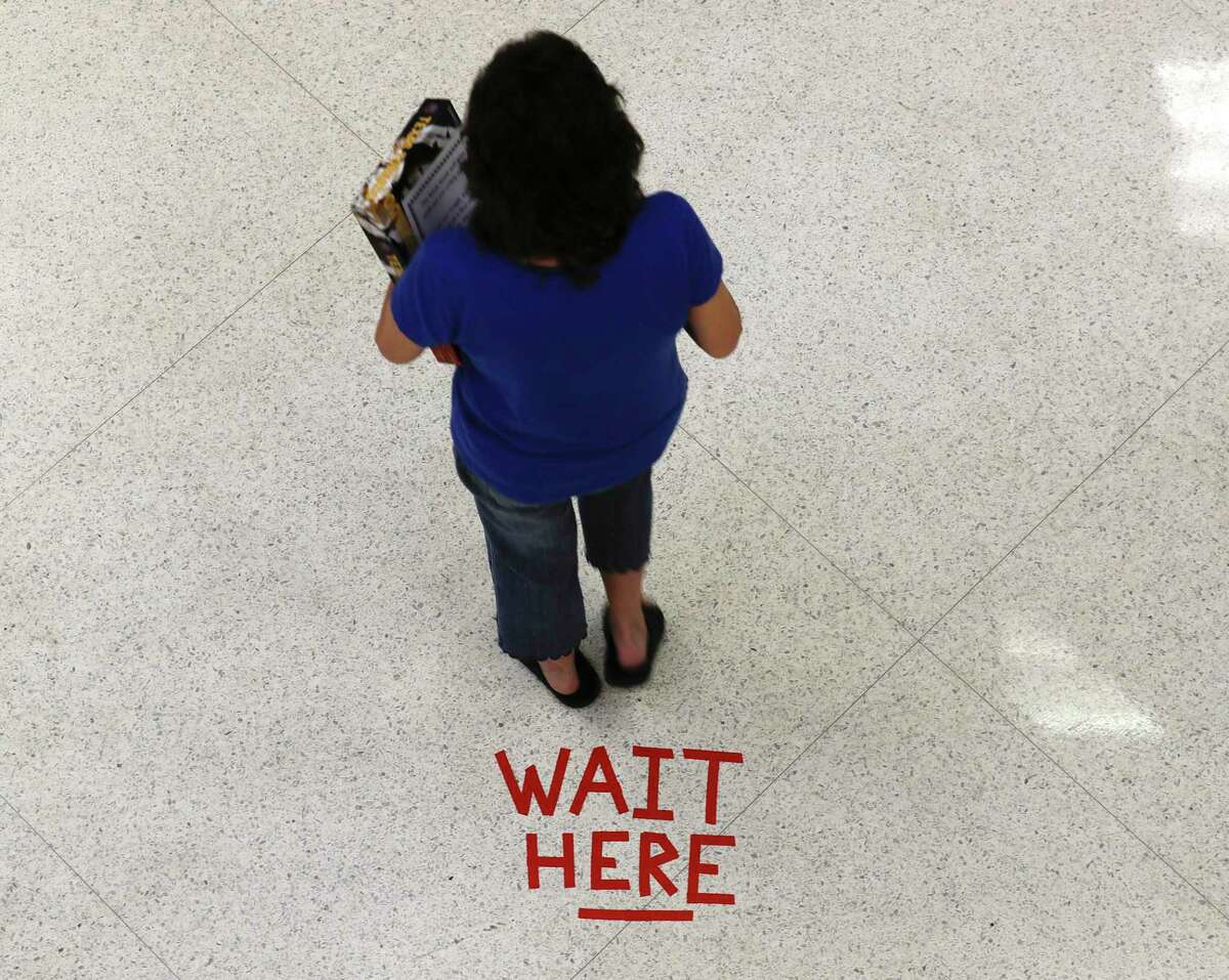 A woman waits in front of a floor marker for social distancing carrying books to check back in as the Montgomery County Central Library reopened to the public, Wednesday, May 13, 2020, in Conroe.