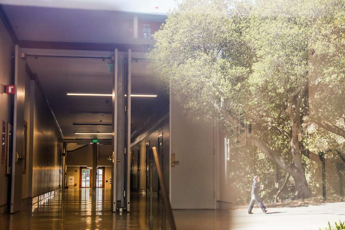 The empty hallway of Wheeler Hall is seen as a person is reflected in a window walking through the UC Berkeley campus on Wednesday, July 8, 2020 in Berkeley, California.