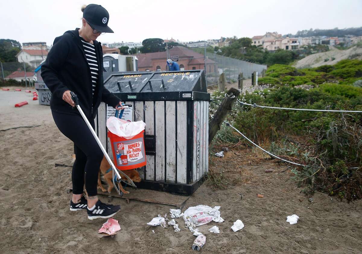 Eva Holman picks up trash and debris left behind by the previous day's visitors in front of the waste bins at Baker Beach in San Francisco, Calif. on Tuesday, June 23, 2020.