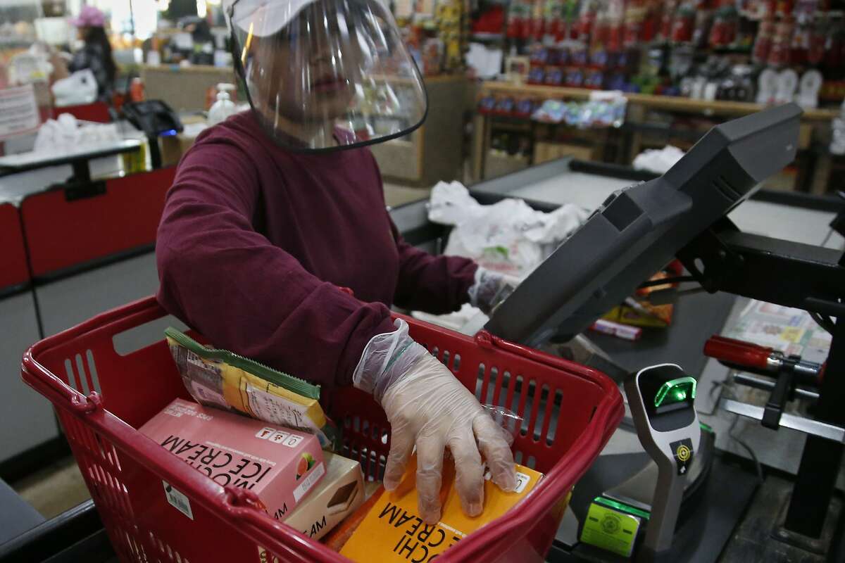 FILE - In this March 27, 2020, file photo, cashier Baby San wears a face shield and gloves as she scans items at grocery store Super Cao Nguyen, in Oklahoma City, due to concerns over the COVID-19 virus. Grocery workers across the globe are working the front lines during lockdowns meant to keep the coronavirus from spreading. (AP Photo/Sue Ogrocki, File)