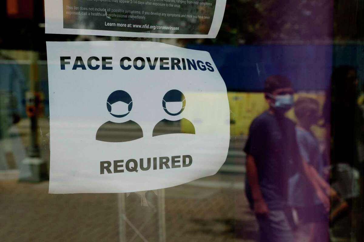 A visitor wearing a masks to protect against the spread of COVID-19 passes a sign requiring masks, Tuesday, July 7, 2020, in San Antonio. Texas Gov. Greg Abbott has declared masks or face coverings must be worn in public across most of the state as local officials across the state say their hospitals are becoming increasingly stretched and are in danger of becoming overrun as cases of the coronavirus surge. (AP Photo/Eric Gay)