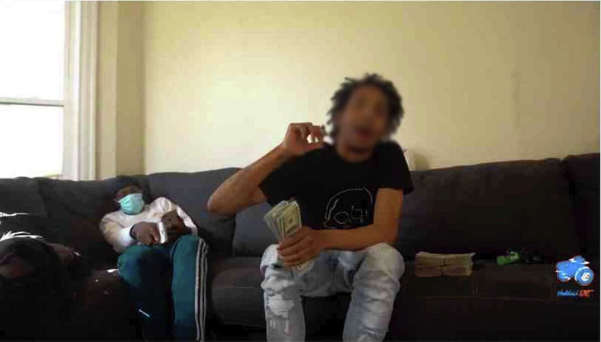 A 17-year-old boy who was convicted in a shooting that injured a toddler in Albany, and later charged with killing a 21-year-old Troy man, had been released under the supervision of probation officials for 11 months due to New York's Raise the Age statute. This photo from a YouTube video showed him holding bundles of cash and smoking marijuana as an unidentified man behind him, wearing a mask, brandished a handgun. The Times Union is not identifying the 17-year-old because he is being prosecuted as an adolescent offender. (Source: Albany County Court records)