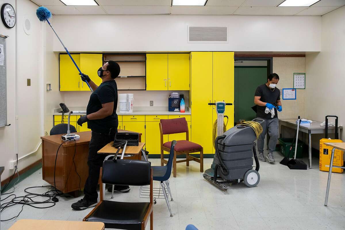 From left: Philip Elliott, the supervising custodian, and custodian Orlando Lavarias clean and sanitize a classroom that will have tables and chairs set up for physical distancing at Westlake Middle School on Friday, July 10, 2020, in Oakland, Calif. Schools are planning on how to reopen in the fall to ensure the safety and wellbeing of students and staff, amid the coronavirus pandemic. The middle school also holds the MetWest High School Ericka Huggins Campus.