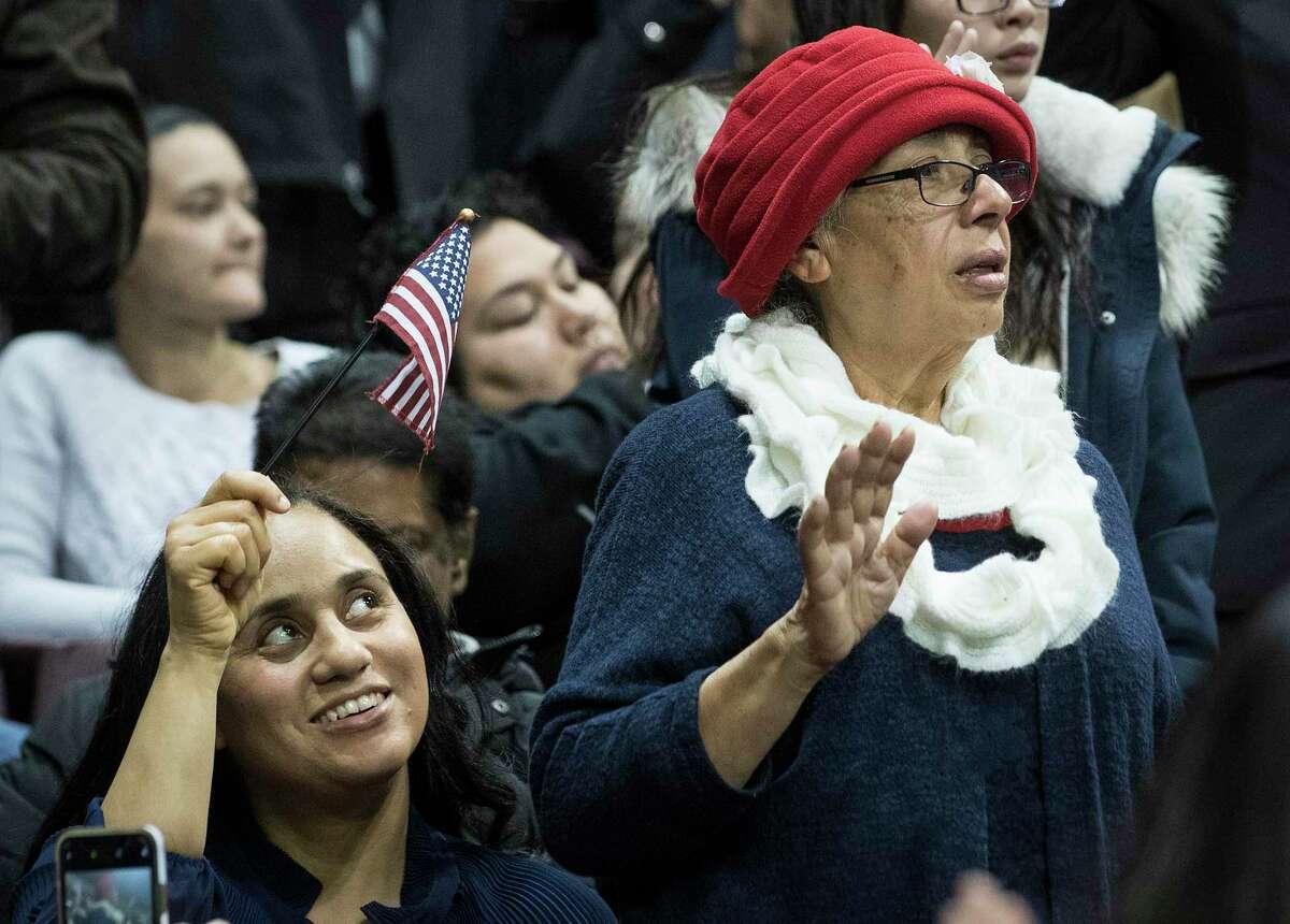 Shirley Smith, left, waves a flag as her mother, Aura Mireles, from Guatemala, takes the oath of allegiance during a naturalization ceremony for more than 2,500 new Americans at the M.O. Campbell Educational Center on Wednesday, Nov. 13, 2019, in Houston. As the state gears up for what could be its most important election in decades, thousands of would-be voters are caught in limbo, stuck in a deep and growing backlog of immigrants applying for U.S. citizenship. While the Trump administration says it is devoting resources to cut down on the backlog, and attorneys in Houston say immigrations officials do appear to be making an effort to get more applications through.