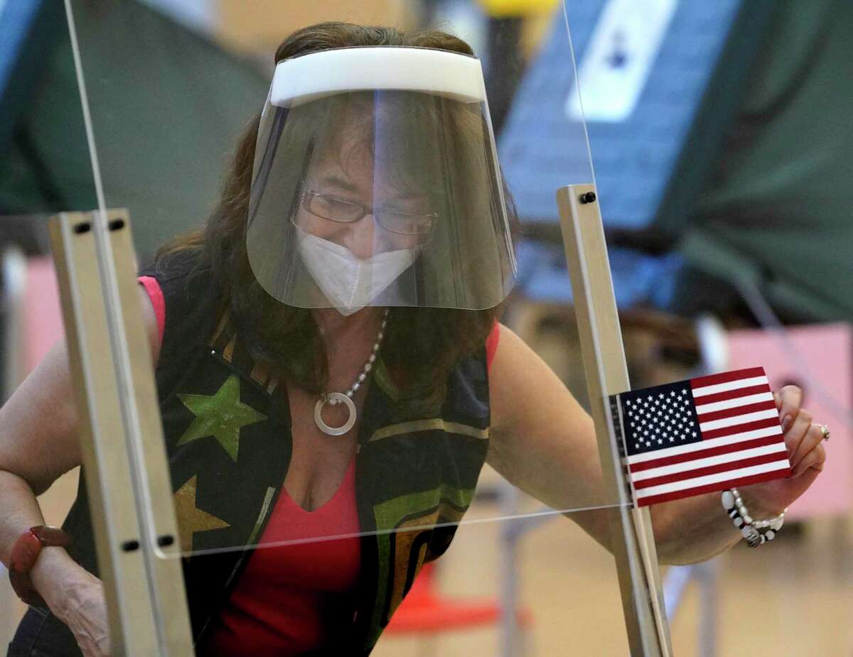 Beatriz Nelson, an election clerk, straightens a flag as she works behind a plastic barrier at her desk wearing a face mask and face shield as people vote at the Metropolitan Multi-Service Center, 1475 West Gray, Friday, July 10, 2020, in Houston.