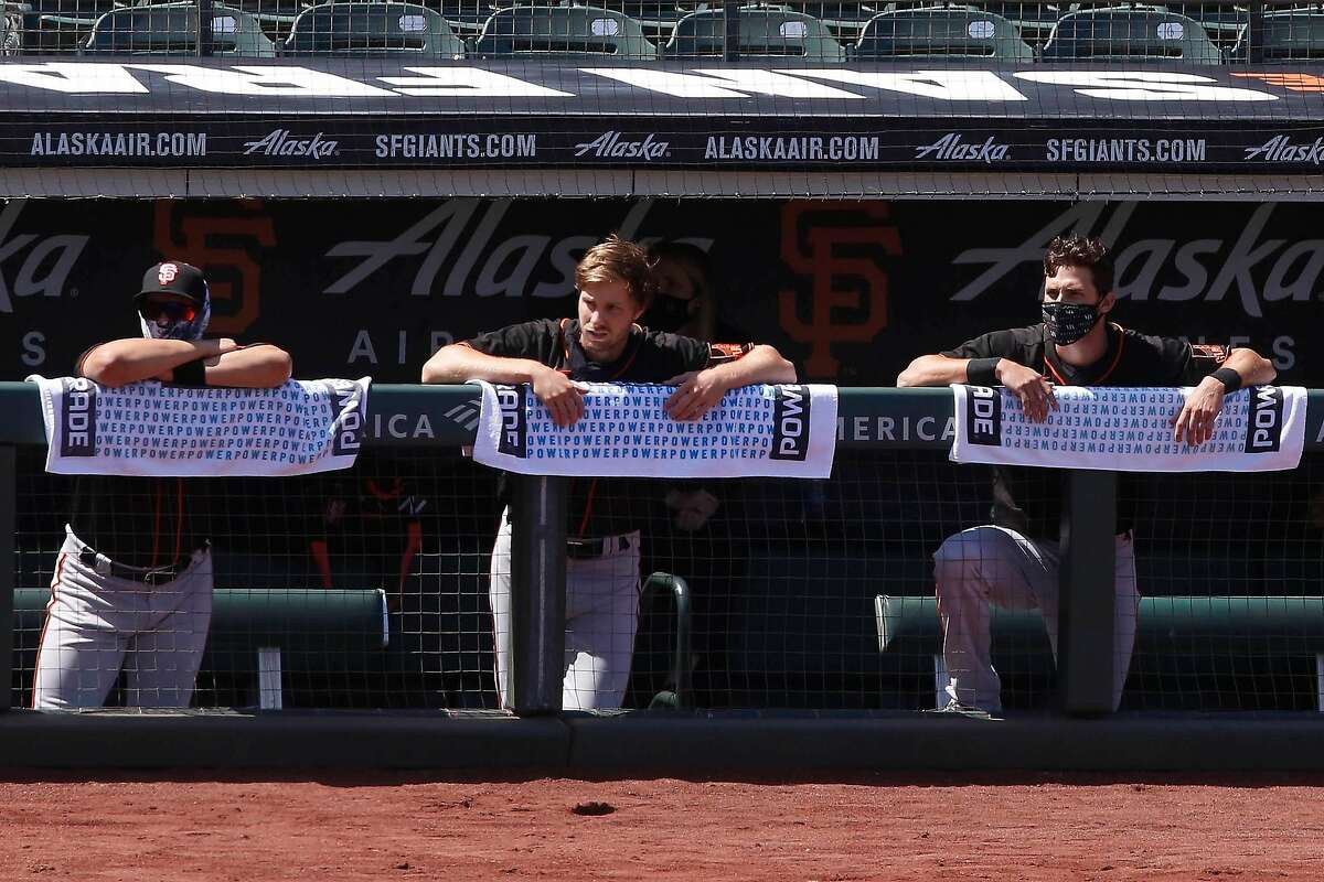 Members of the San Francisco Giants lean on towels as they watch practice from the dugout at Oracle Park in front of rows of empty seats on Monday, July 13, 2020 in San Francisco, Calif.