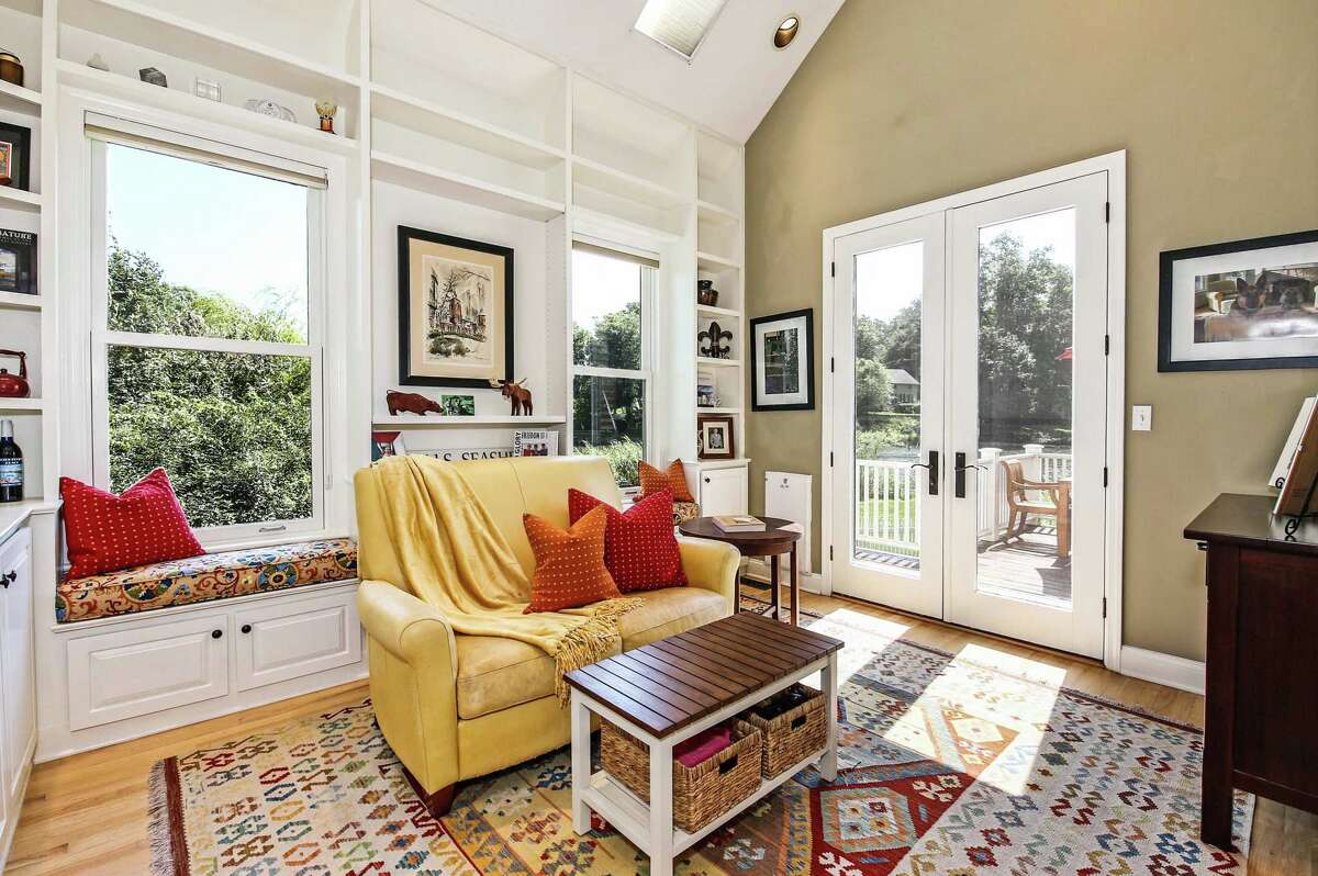 Inside this house there is an open floor plan, which enhances the water views, and contemporary colors. The walls are painted in neutral earth tones, putting it ahead of the curve as many Fairfield County homes are transitioning away from monochromatic grays to shades of beige and green. The living room has a fieldstone fireplace, tall double-hung windows, and French doors to the large wrap-around deck. The den has a vaulted ceiling, two walls of floor-to-ceiling built-in shelving and cabinets, a window seat, and French doors to the deck.