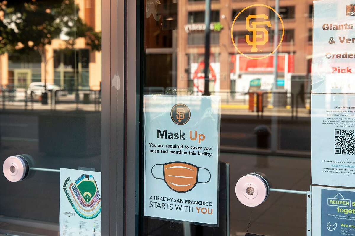 A sign reminds patrons to wear a mask while a hand sanitizer dispenser sits nearby as the San Francisco Giants' begin their summer training camp session at Oracle Park in San Francisco, Calif. Saturday, July 4, 2020. Due to COVID-19, the 2020 MLB season has been postponed with players just beginning to return for warmups and practices while wearing masks and keeping social distance.