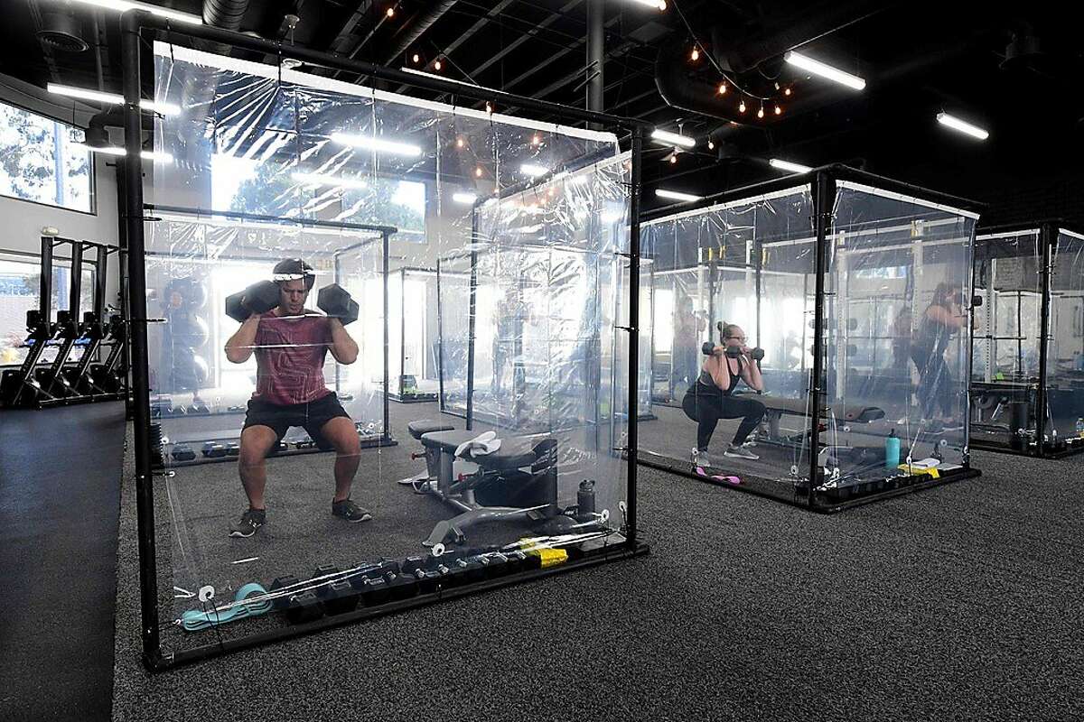 (FILES) In this file photo taken on June 16, 2020 people exercise at Inspire South Bay Fitness behind plastic sheets in their workout pods while observing social distancing in Redondo Beach, California, as the gym reopens today under California's coronavirus Phase 3 reopening guidelines. (Photo by FREDERIC J. BROWN / AFP) (Photo by FREDERIC J. BROWN/AFP via Getty Images)
