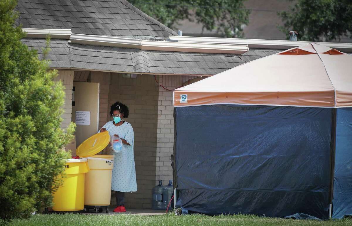 A woman disposes of a plastic bag in a yellow container in a hospital gown and gloves as PPE equipment at the Windsong Care Center Thursday, July 16, 2020, in Pearland.