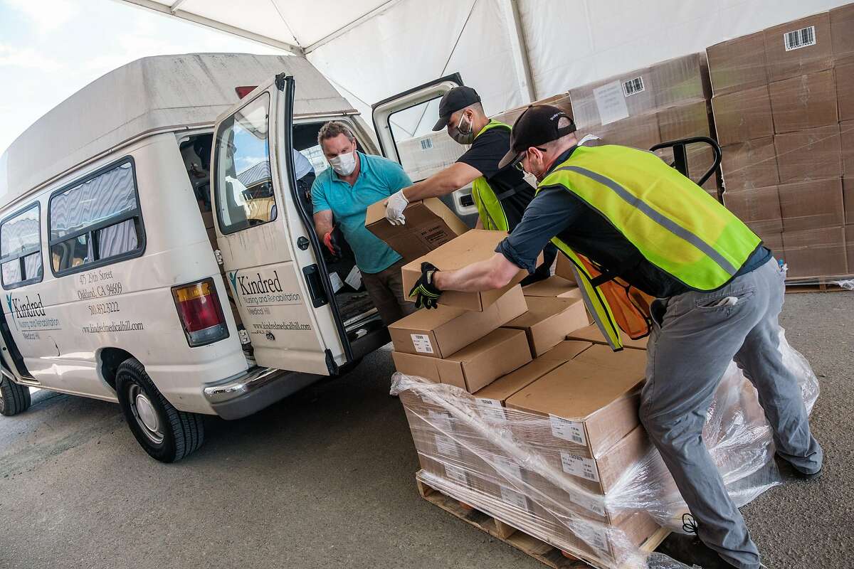 Daniel Flores and Frank Vickers in green vests, help load a vehicle with gowns, masks and other PPE at the Alameda County emergency services warehouse in Dublin on Friday, July 10, 2020.