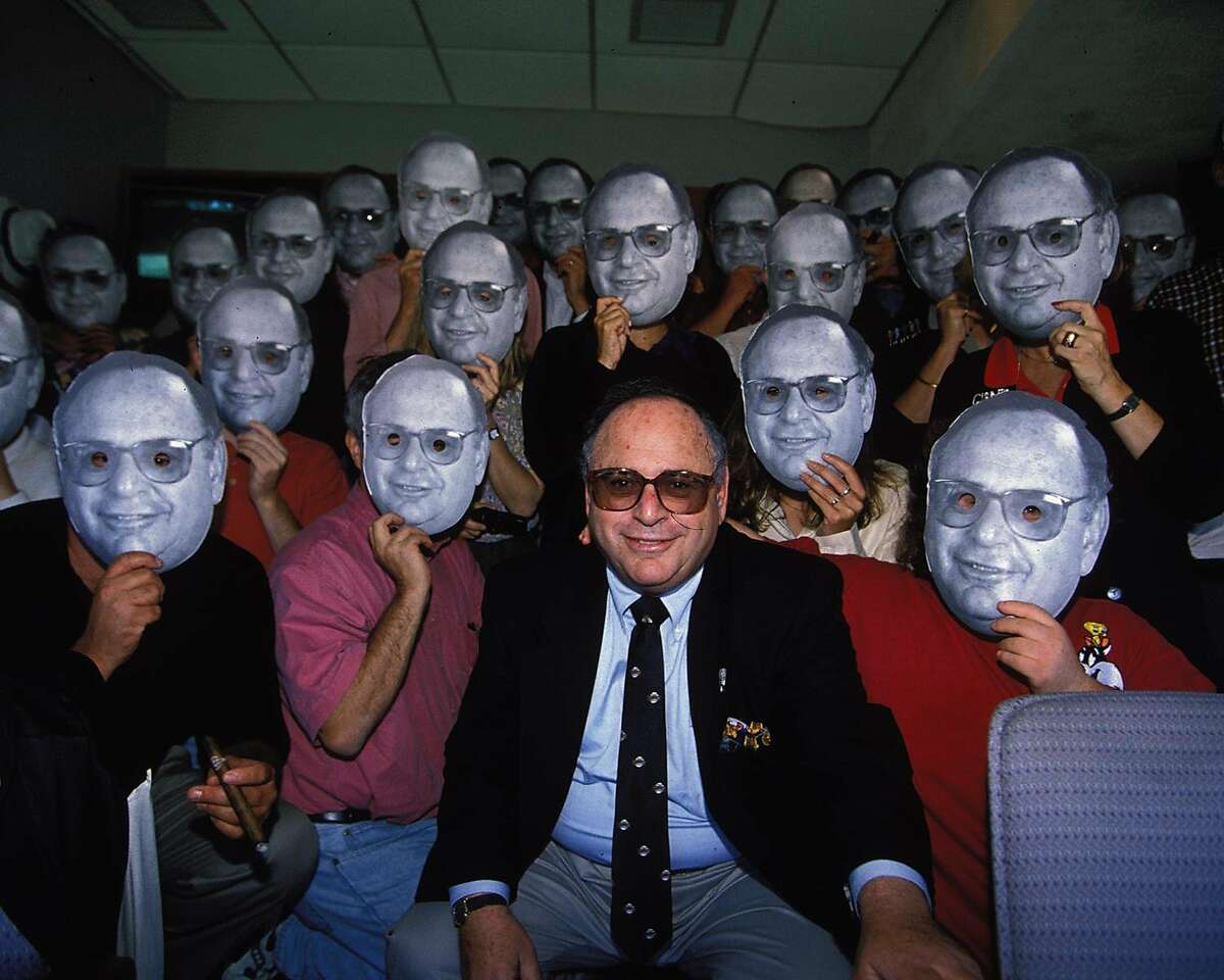 Hank Greenwald sits in the center of a group photo from his birthday party, surrounded by guests holding up cardboard cutouts of his face.
