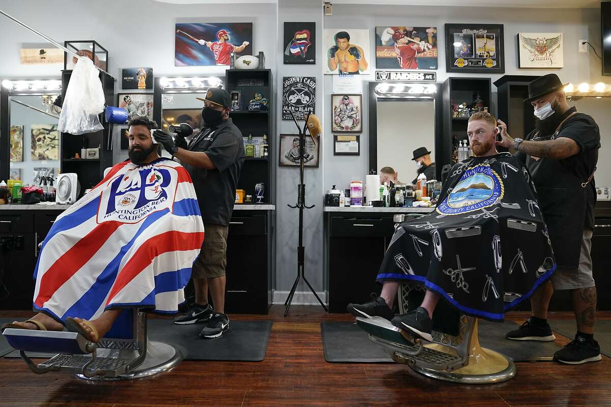 Ricardo Rivera, left, has his hair cut by Anthony Acosta while Braunson McDonald has his hair cut by Luis Lopez, right, owner of Orange County Barbers Parlor, Wednesday, July 15, 2020, in Huntington Beach, Calif. California Gov. Gavin Newsom this week ordered that indoor businesses like salons, barber shops, restaurants, movie theaters, museums and others close due to the spread of COVID-19. (AP Photo/Ashley Landis)