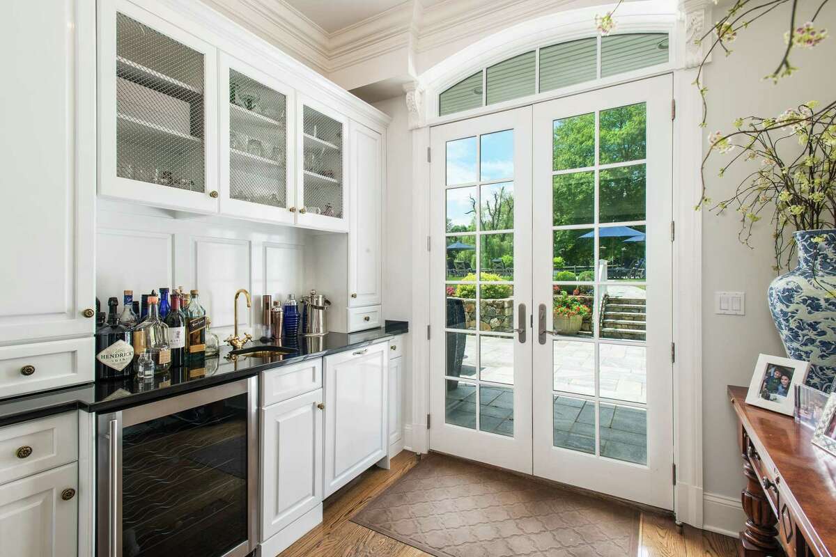 Entertaining outside is enhanced by an interior wet bar with a granite counter, glass-front cabinetry, a beverage refrigerator and French doors that open to the patio. A wide stone path brings visitors to the covered front entrance comprising French doors framed by ivy-covered stone. Those doors open into the true center hall, which peers through the rear multi-paned glass French doors into the backyard.