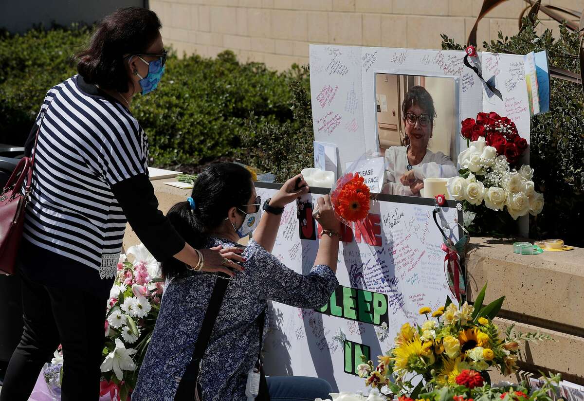 Nurse Jennie S-M (did not give full last name) signs a memorial as colleague Vessie Tacla supports her during a vigil for nurse Janine Paiste-Ponder, who died of COVID-19 after working with patients with the disease at Alta Bates Summit Medical Center in Oakland , Calif., on Tuesday, July 21, 2020. Colleagues will remembered the nurse of more than 25 years at a vigil Tuesday. They said she didn’t sign up to sacrifice her life, and called upon the hospital to provide more protective equipment and testing after exposure to patients. Across California, 19,734 health care workers have tested positive and 107 have died.