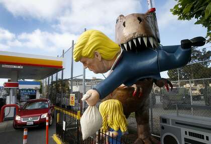 Drivers leaving the virtual reality video car wash at a Shell gas station and car wash in San Bruno are greeted by a satirical sculpture of a T-Rex eating President Trump.