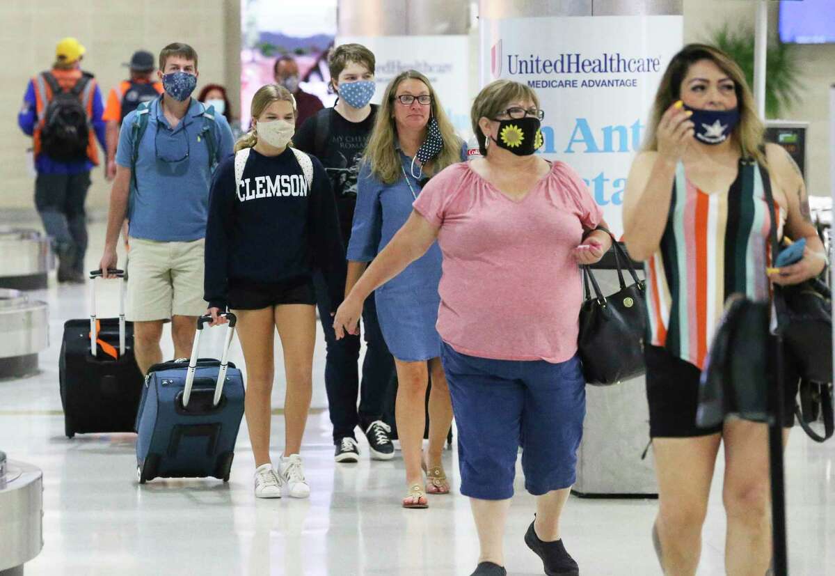 Passengers move about in the San Antonio International Airport terminals, passing by numerous signs indicating mask requirements on July 22, 2020.