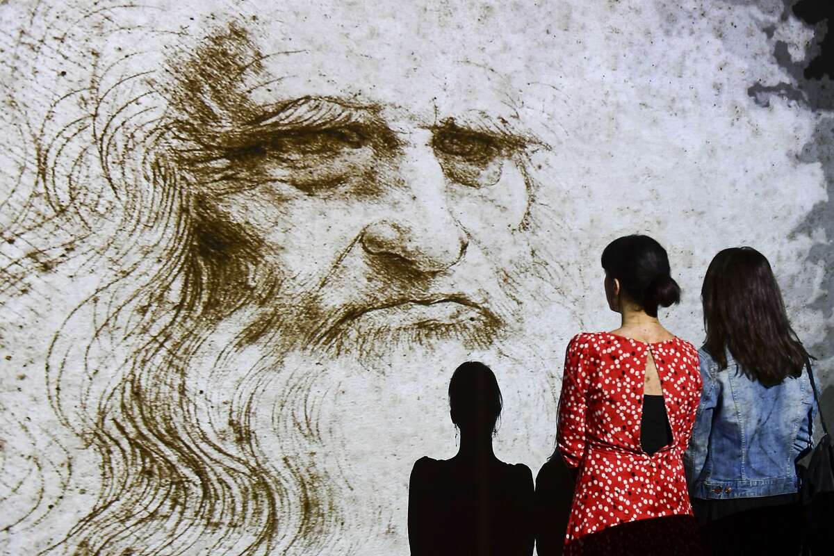 People watch a hologram called "Studio di uomo barbuto" (study of bearded man) during the Leonardo da Vinci multimedia installation "Leonardo Da Vinci 3D" at the Fabbrica del Vapore (Steam Factory) in Milan, on May 29, 2019. - The exhibition taking place from May 30 to September 22, 2019, breaks through traditional art exhibition boundaries, challenging the laws of physics, time and space with lights, images, sounds and colors. 2019 marks the 500th anniversary of the death of the artist and inventor. (Photo by Miguel MEDINA / AFP) / RESTRICTED TO EDITORIAL USE - MANDATORY MENTION OF THE ARTIST UPON PUBLICATION - TO ILLUSTRATE THE EVENT AS SPECIFIED IN THE CAPTION (Photo credit should read MIGUEL MEDINA/AFP via Getty Images)