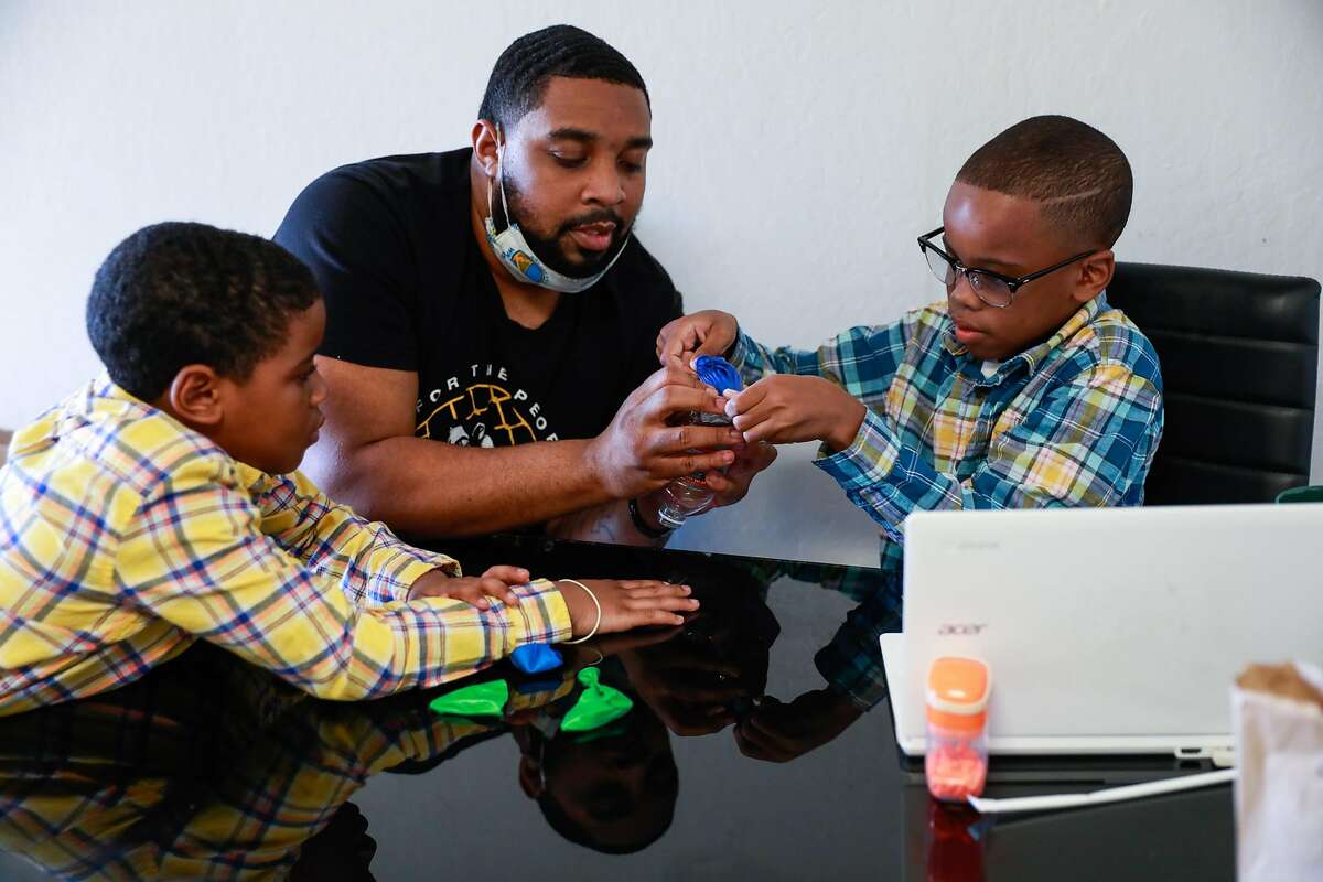 James Thomas helps his son Jamal Lee Jr.,10, (right) recreate a lung with a balloon and plastic bottle during an online science class as his other son Javaughn Thomas, 7, looks on on Wednesday, July 22, 2020 in San Leandro, California.