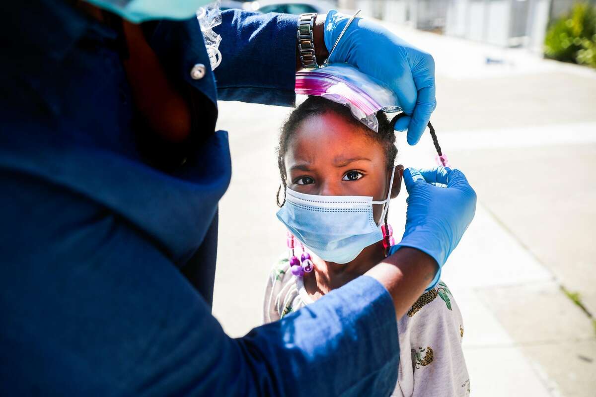 (L-r) Janice Smith helps London Gilbert, 5 put on her mask on Thursday, May 7, 2020 in San Francisco, California. The Community Resilience Caravans, which were organized through the city, canvassed neighborhoods throughout District 10 to encourage social distancing and hand out masks amid the coronavirus pandemic.