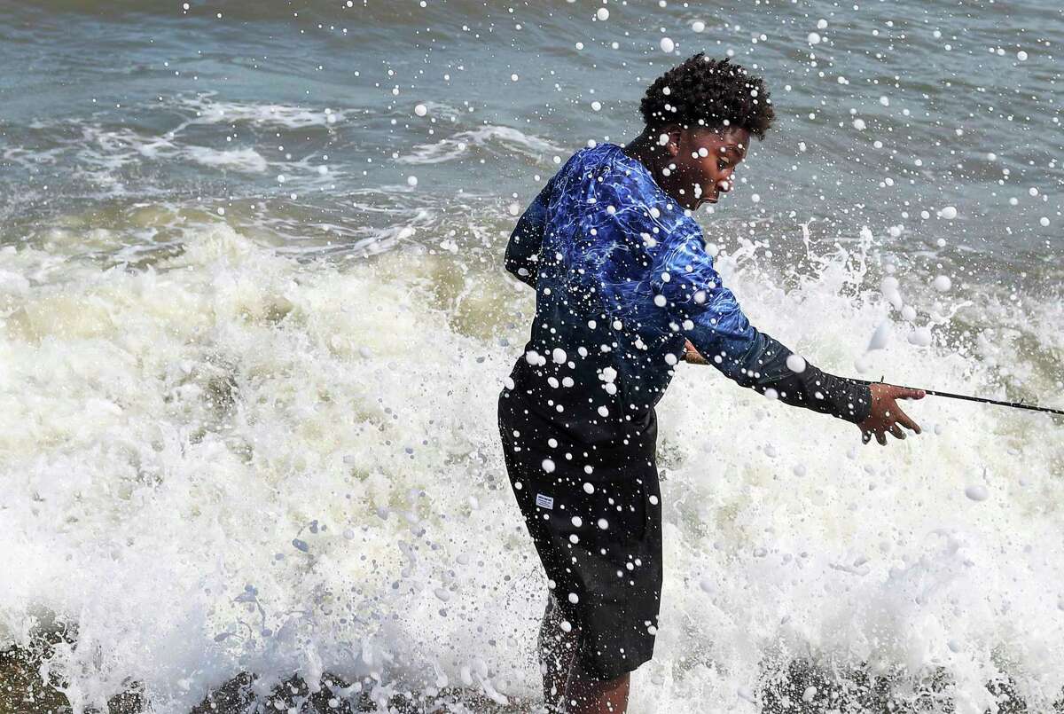 Jaden Simmons, 14, reacts as he is hit by a wave while fishing at the end of a jetty Thursday, July 23, 2020, at the beach in Galveston. "I hope the big one doesn't come," he said shortly before.