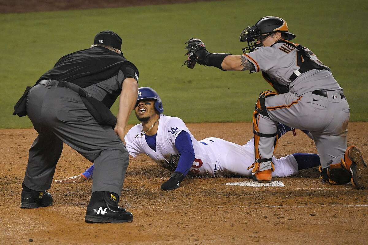 Los Angeles Dodgers' Mookie Betts, center, scores on a fielder's choice hit by Justin Turner as San Francisco Giants catcher Tyler Heineman takes a late throw and home plate umpire Bill Miller makes the call during the seventh inning of an opening day baseball game, Thursday, July 23, 2020, in Los Angeles. (AP Photo/Mark J. Terrill)