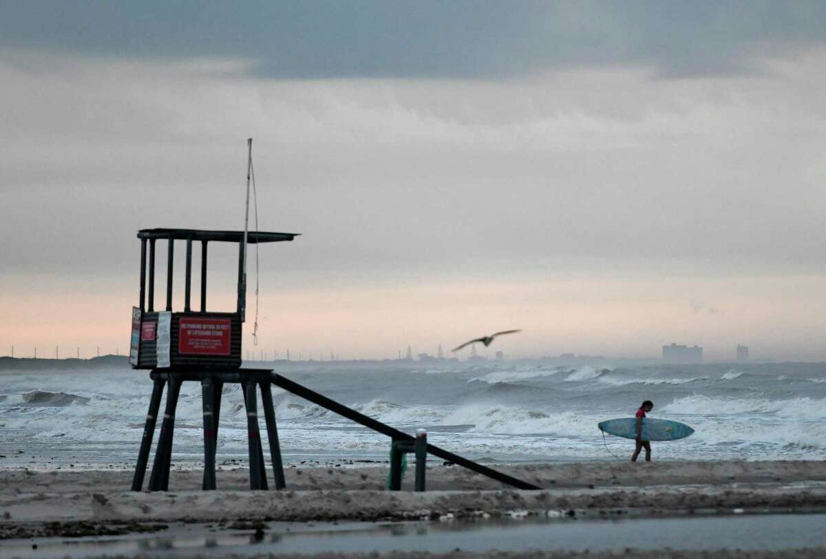 A surfer walks on the beach at J.P. Luby Park ahead of Tropical Storm Hanna, Friday, July 24, 2020, in Corpus Christi, Texas. The storm is expected to make landfall on Saturday. (Annie Rice/Corpus Christi Caller-Times via AP)