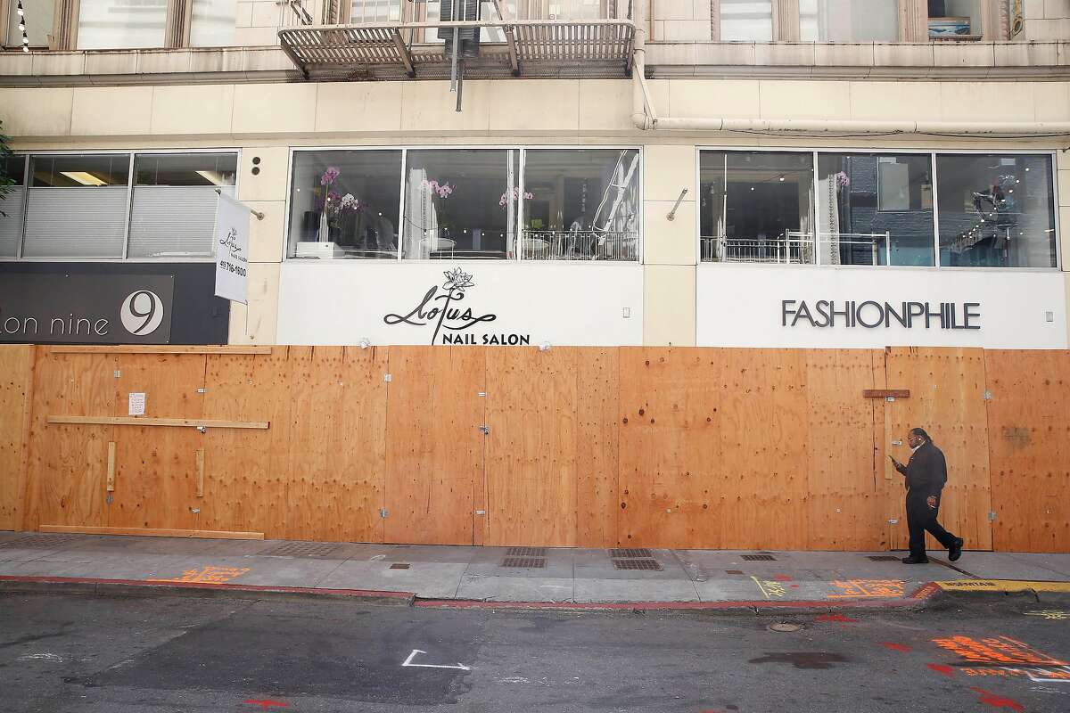 Keithe Ubedei of Oakland walks past a boarded up stores on Maiden Lane on Wednesday, July 8, 2020 in San Francisco, Calif.
