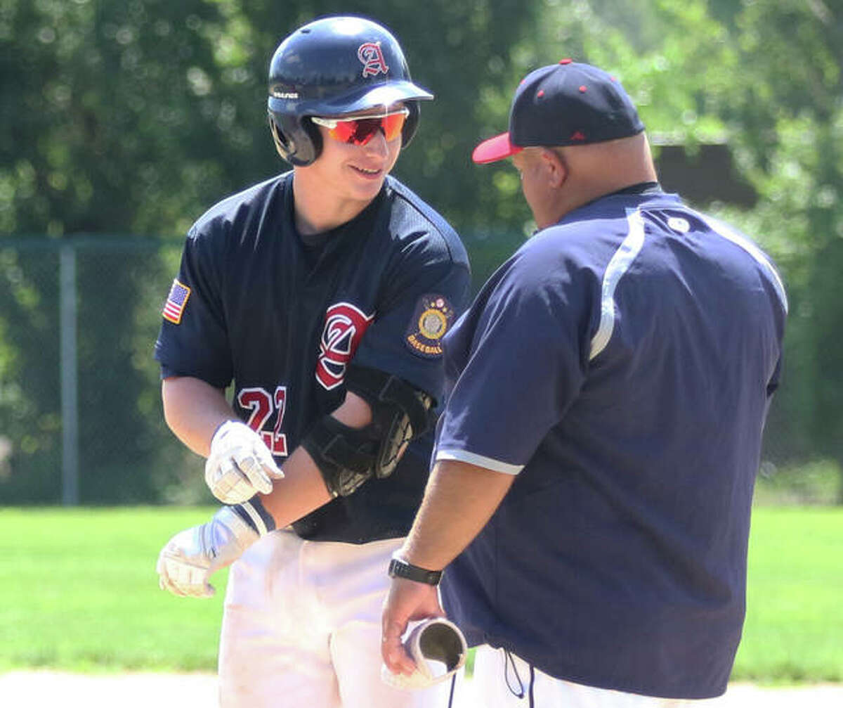 Alton’s Cullen McBride (left) talks with first base coach Brian Hanslow after McBride’s RBI single in the third inning Saturday at Hopkins Field in Alton.